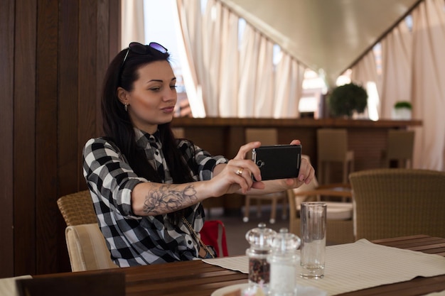 Mooie vrouw met een tatoeage en geruit overhemd doet selfie op tafel in een prachtig café.