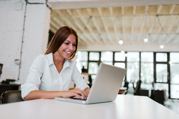 Mooie vrouw met een toothy glimlach die aan laptop in modern bureau werkt.