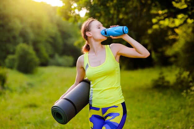 Mooie vrouw met een yogamat in openlucht in park op zonsondergang