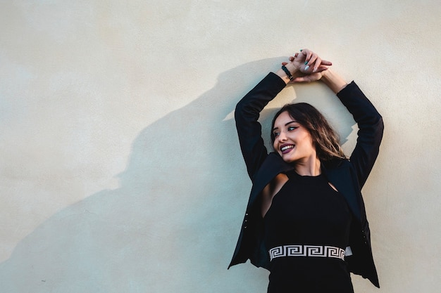 Mooie vrouw met elegante kleding poseren ontspannen op de muur.