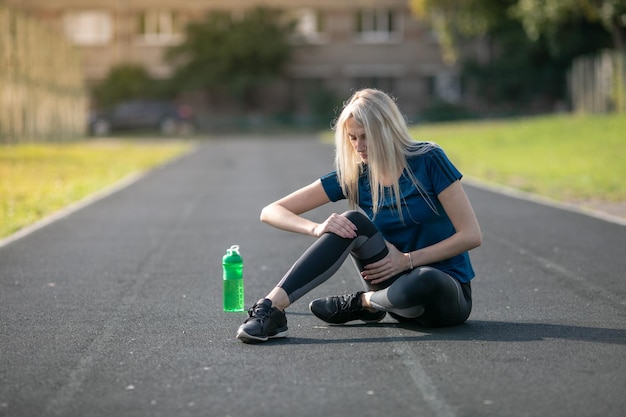 Mooie vrouw met enkelblessure in atletiekbaan., Gezondheidszorg en sportconcept. groene bidon om te drinken