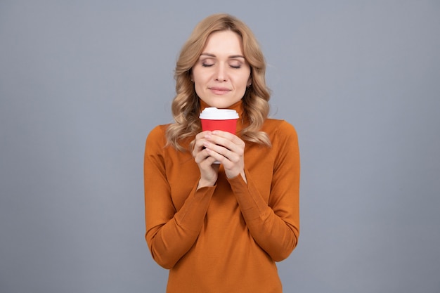 Mooie vrouw met gesloten ogen geniet van de geur van vers gezette thee of koffie grijze achtergrond, genietend van het leven.