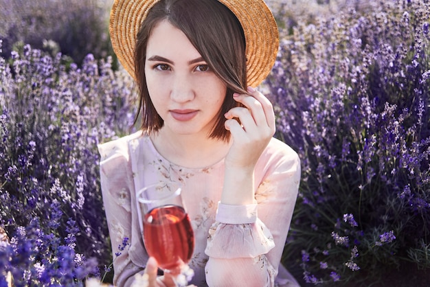 Foto mooie vrouw met glas wijn in lavendelvelden. het meisje in strohoed ontspant op picknick