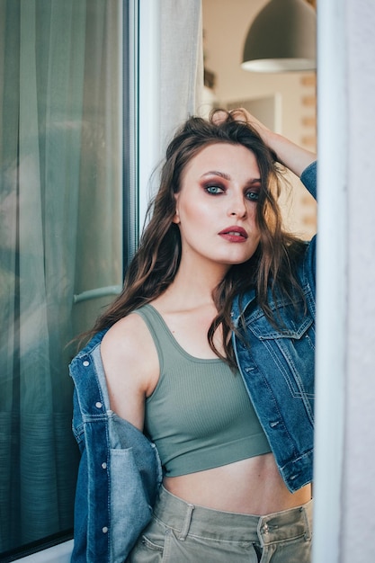 Mooie vrouw met golvend haar en professionele make-up in een spijkerjasje poseren in een studio of kamer.