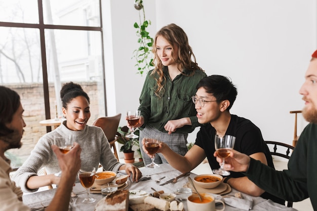 Mooie vrouw met golvend haar glas wijn in de hand houden permanent in de buurt van tafel vol met eten