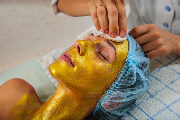 Mooie vrouw met gouden gezichtsmasker bij schoonheidssalon