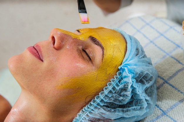 Mooie vrouw met gouden gezichtsmasker bij schoonheidssalon