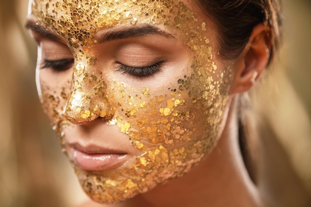 Mooie vrouw met gouden glanzend masker op haar gezicht voor huidbehandeling