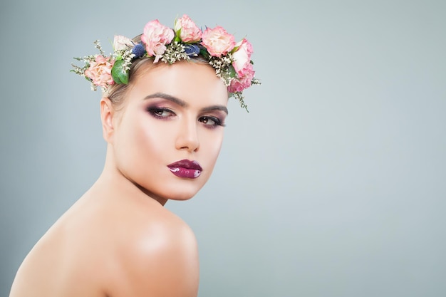 Mooie vrouw met kleurrijke make-up in een krans van bloemen en bladeren op lichtblauwe achtergrond met kopieerruimte