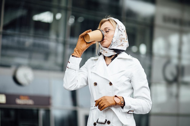 Mooie vrouw met koffiekopje in de buurt van kantoorgebouw.