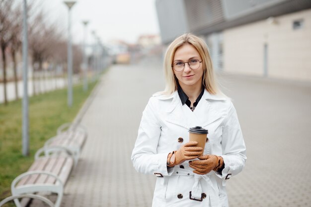 Mooie vrouw met koffiekopje in de buurt van kantoorgebouw.