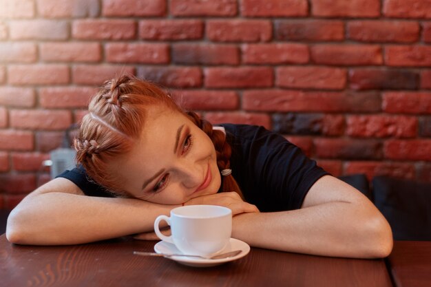 Mooie vrouw met kopje koffie ligt op tafel en kijkt glimlachend opzij