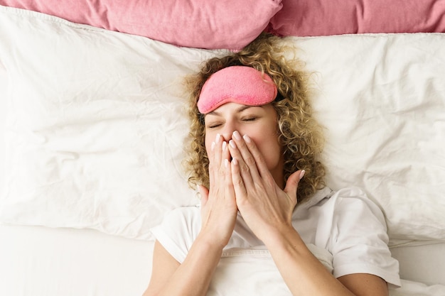 Mooie vrouw met krullend haar die wakker wordt na een goede nachtrust in een slaapkamer