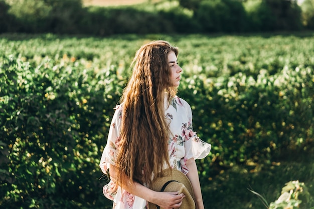 Mooie vrouw met lang krullend haar en sproeten gezicht op bes veld achtergrond. Meisje in een lichte jurk wandelingen in de zonnige zomerdag