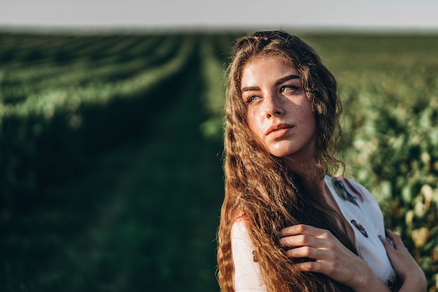 Mooie vrouw met lang krullend haar en sproetengezicht op besgebied. Het meisje in een lichte kleding loopt in de zonnige zomerdag