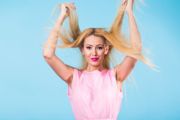 Mooie vrouw met lang recht blond haar. Mannequin poseren op blauwe muur