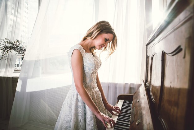 Mooie vrouw met mooie elegante jurk poseren in de pianokamer