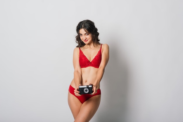 Mooie vrouw met mooie glimlach in rode lingerie pinup stijl met fotocamera, geïsoleerd op wit