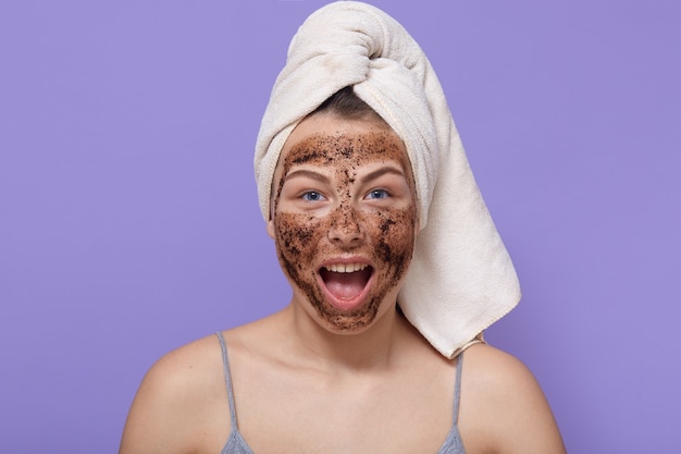 Mooie vrouw met mouwloos t-shirt en gewikkelde handdoek verlaten, cosmetische ingrepen doen om de huid te pellen