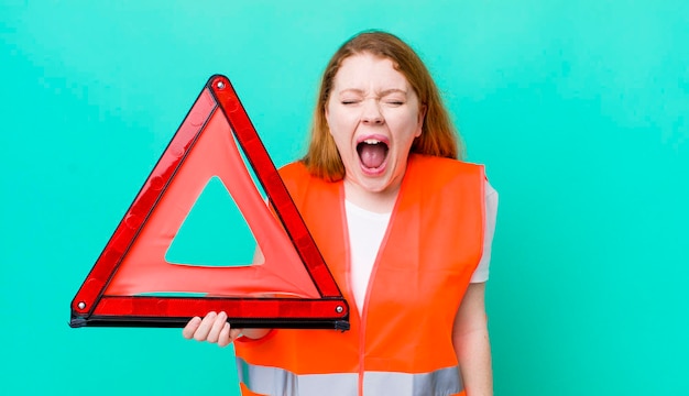 Mooie vrouw met rood hoofd die agressief schreeuwt en er erg boos uitziet met een auto-driehoekongeval