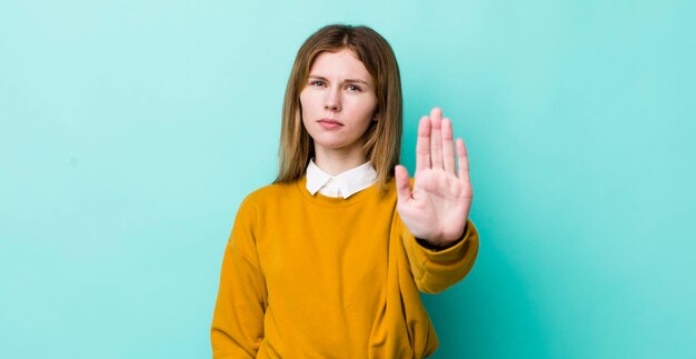 Mooie vrouw met rood hoofd die er ernstig streng uitziet, ontevreden en boos met open palm die een stopgebaar maakt