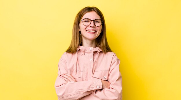 Mooie vrouw met rood hoofd die eruitziet als een gelukkige trotse en tevreden presteerder die lacht met gekruiste armen