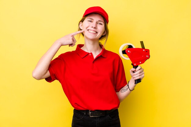 Mooie vrouw met rood hoofd die lacht en vol vertrouwen wijst naar het concept van de brede glimlachverpakker