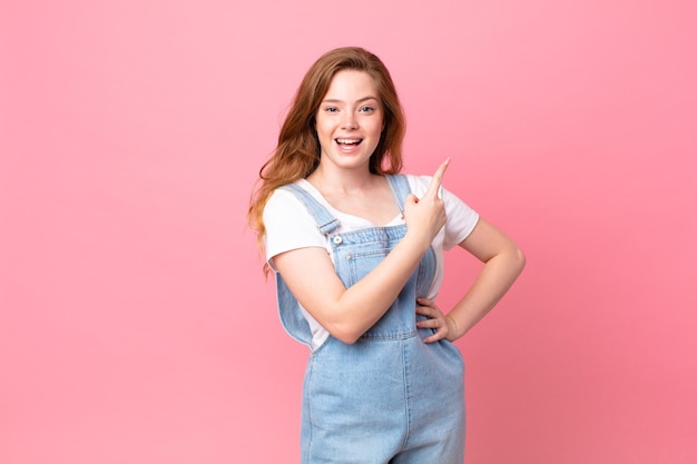 Mooie vrouw met rood hoofd die opgewonden en verrast kijkt en naar de zijkant wijst