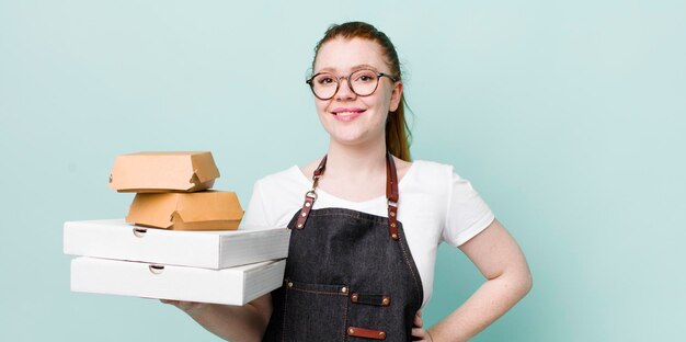 Mooie vrouw met rood hoofd die vrolijk lacht met een hand op de heup en zelfverzekerd afhaalconcept