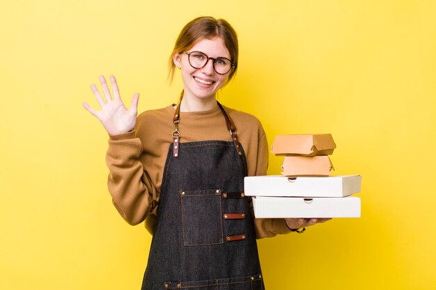 Mooie vrouw met rood hoofd lacht en ziet er vriendelijk uit en toont nummer vijf fast food take away tender