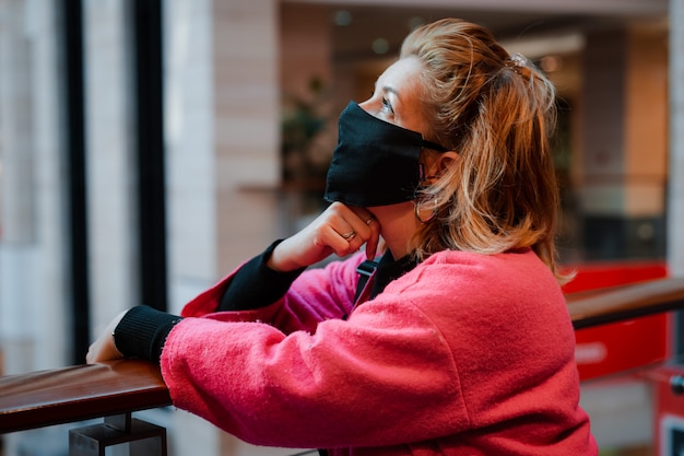 Mooie vrouw met telefoon helder roze winkelcentrum jas met zwarte beschermend masker