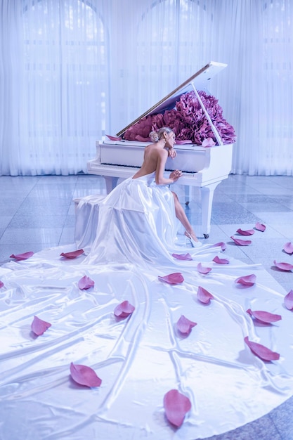 Mooie vrouw met witte piano en pioenrozen bloemen in witte studio