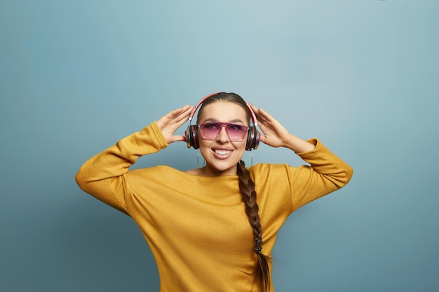 Mooie vrouw met zonnebril in gele trui die muziek luistert met draadloze koptelefoon