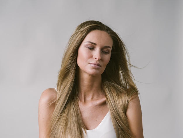 Mooie vrouw natuurlijke portret meisje met lang blond haar over wit grijze muur. Studio opname.