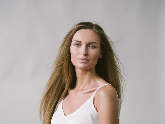 Mooie vrouw natuurlijke portret meisje met lang blond haar over wit grijze muur. Studio opname.