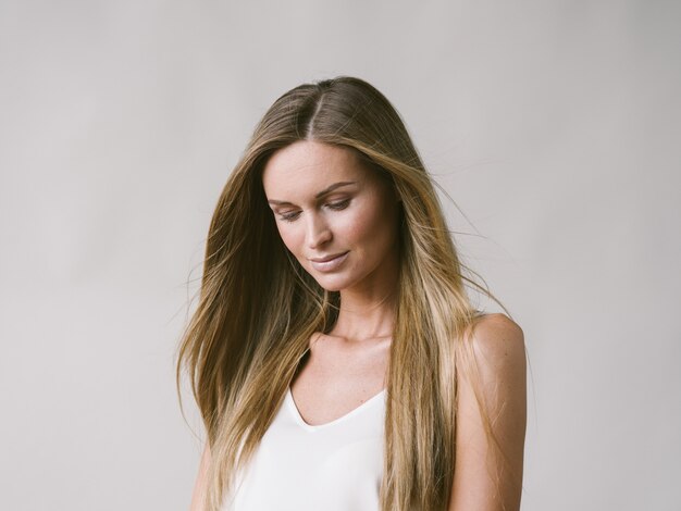 Mooie vrouw natuurlijke portret meisje met lang blond haar over wit grijze muur. Studio opname.