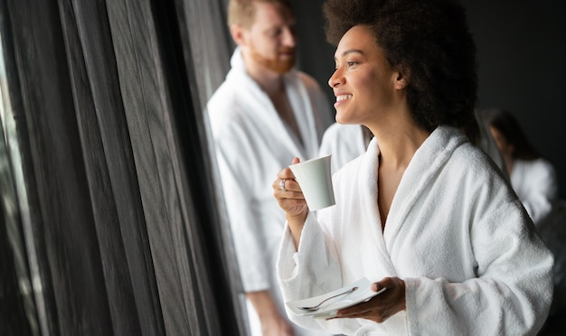 Mooie vrouw ontspannen in luxe hotel spa met een badjas die naar het raam kijkt en koffie drinkt