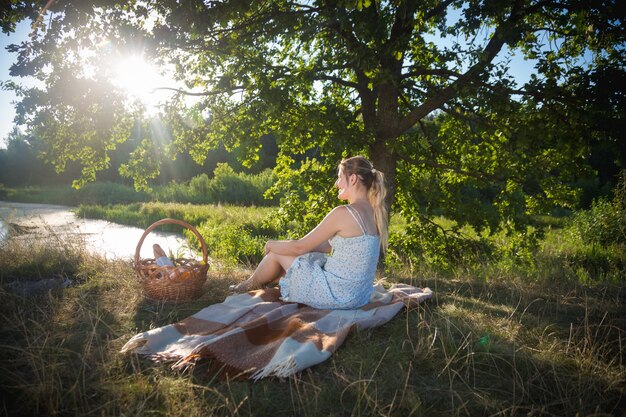 Mooie vrouw ontspannen op deken onder boom en kijken naar zonsondergang