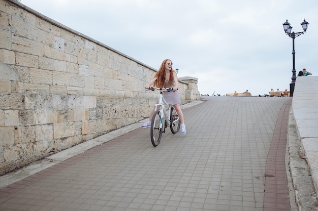 Mooie vrouw op de fiets Lifestyle en gezondheid in de stad Vrolijke roodharige jonge vrouw krijgt plezier van wandelen door de stad