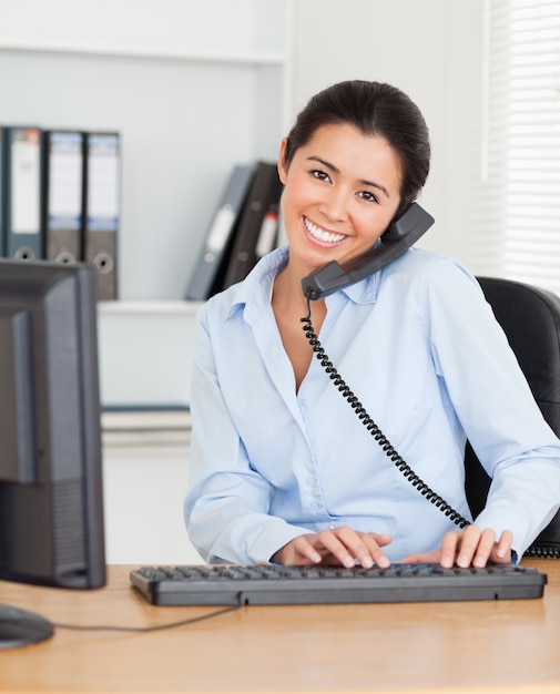 Mooie vrouw op de telefoon tijdens het typen op een toetsenbord