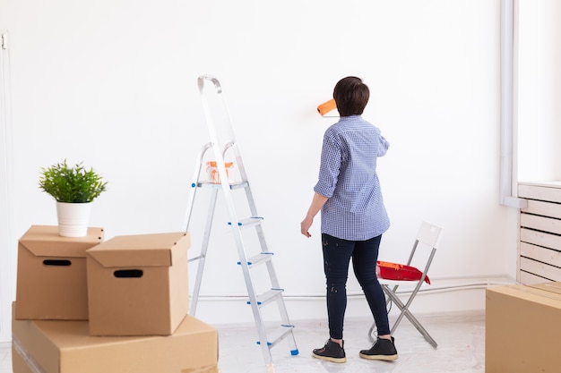 Mooie vrouw op middelbare leeftijd schilderen muur in haar nieuwe appartement. renovatie en herinrichting concept.