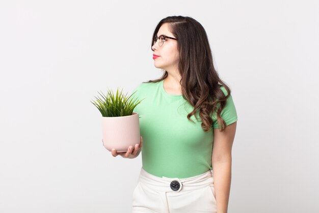 Mooie vrouw op profielweergave denken, verbeelden of dagdromen en een decoratieve plant vasthouden