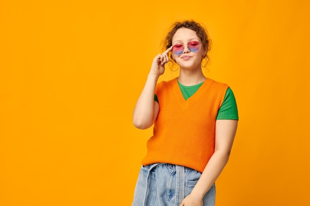 Mooie vrouw oranje sweatshirts zonnebril veelkleurige glazen leveren gele achtergrond ongewijzigd