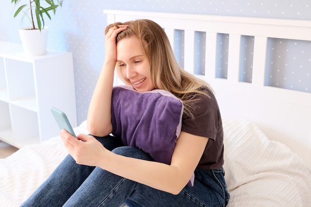 mooie vrouw poseren zittend op het bed met een smartphone in haar handen