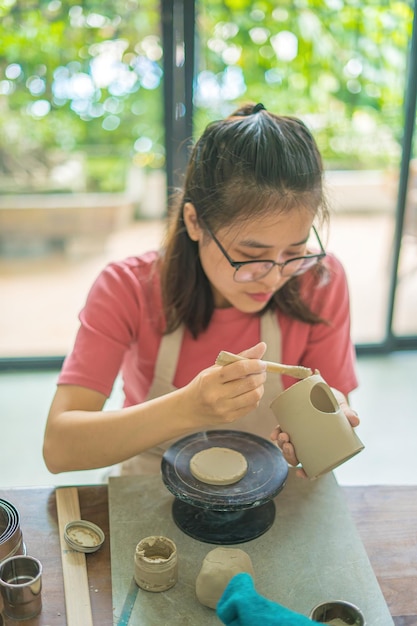 Mooie vrouw pottenbakker bezig met pottenbakkers wiel maken van keramische pot van klei in aardewerk workshop Focus hand jonge vrouw klei product onderdeel vastmaken aan toekomstig keramisch product Aardewerk workshop