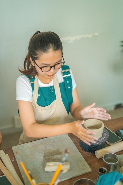 Mooie vrouw pottenbakker bezig met pottenbakkers wiel maken van keramische pot van klei in aardewerk workshop Focus hand jonge vrouw klei product onderdeel vastmaken aan toekomstig keramisch product Aardewerk workshop