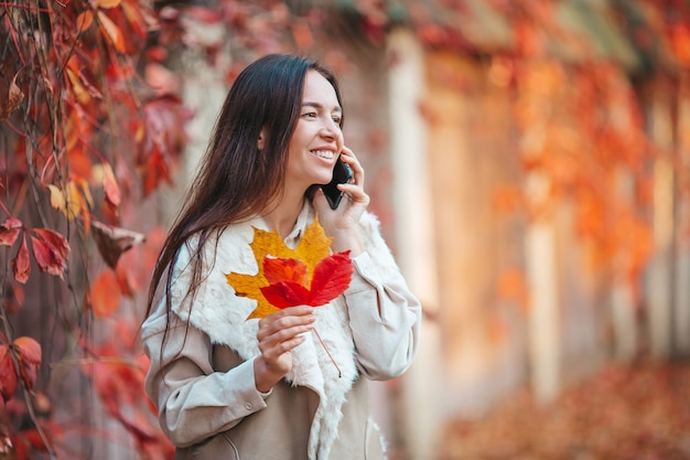 Mooie vrouw praten via de telefoon in herfst park onder bladeren vallen.