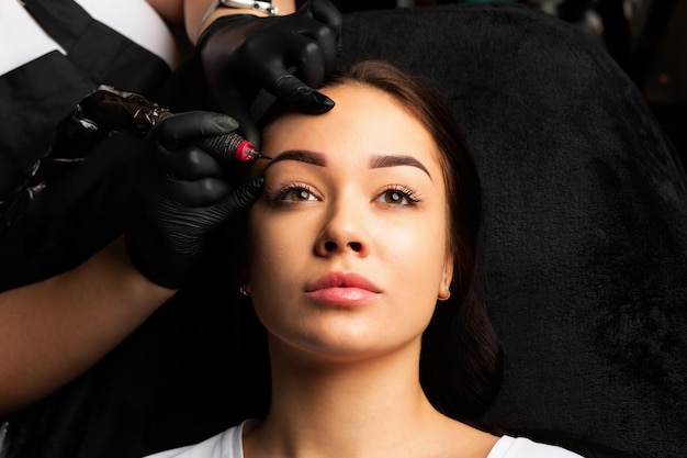 Foto mooie vrouw procedure van permanente wenkbrauw make-up ondergaan in tattoo salon