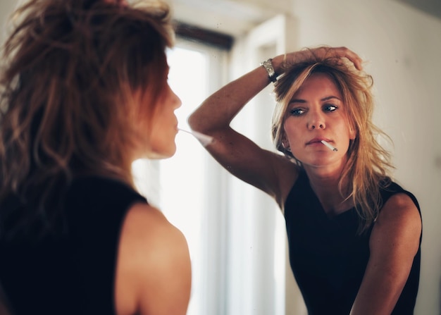 Mooie vrouw rookt een sigaret terwijl ze voor de spiegel staat