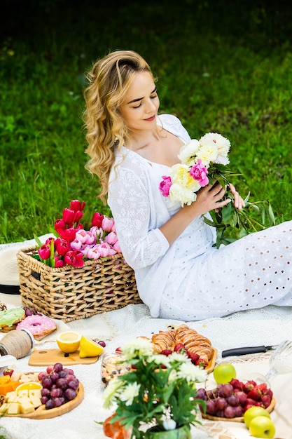 Mooie vrouw rustend in het park zittend op een picknickdeken met fruit en wijn